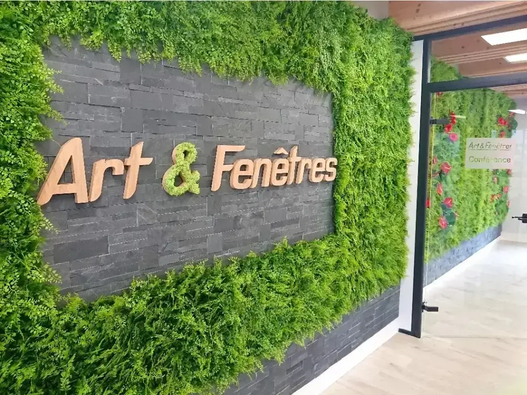 Mur végétal d'intérieur artificiel et stabilisé sur mesure avec intégration du logo personnalisé de l'enseigne Art & Fenêtres dans un espace professionnel avec prolongation en salle de conférence par Cindy Gunther