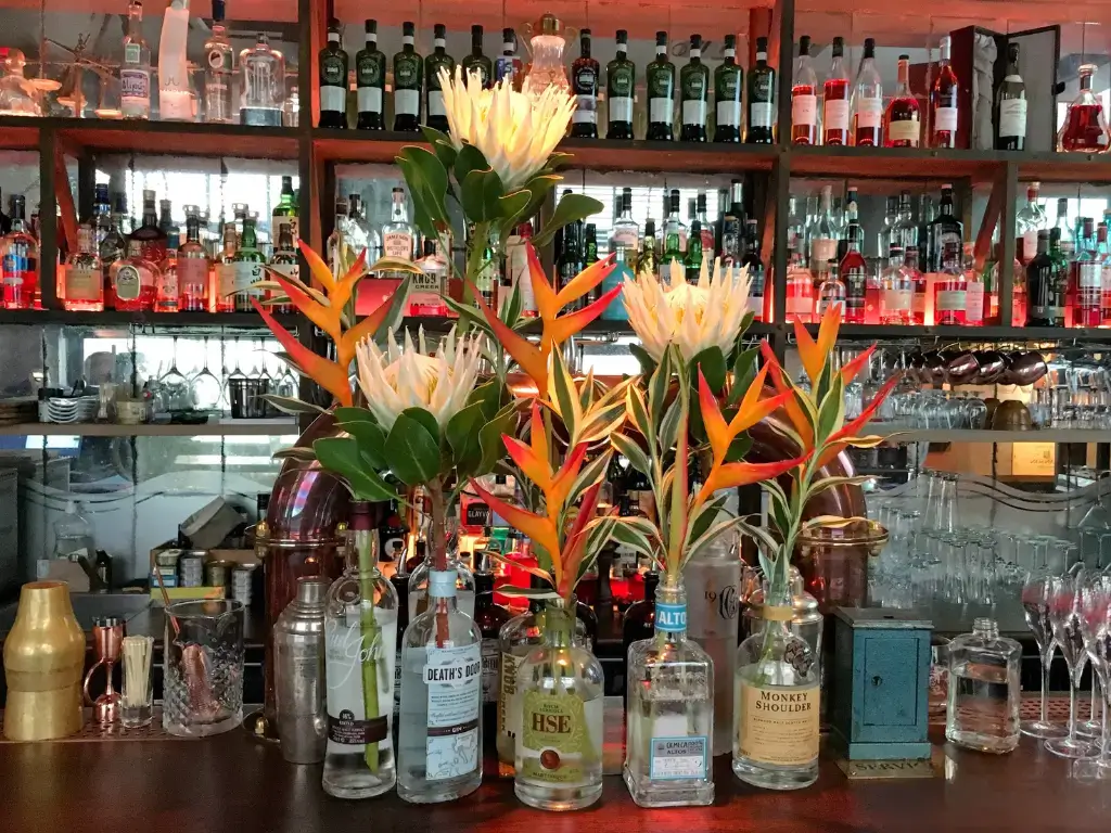 Composition de fleurs exotiques luxueuses dans des bouteilles d'alcool d'exception pour le Bar 1919 à Paris. par Cindy Gunther