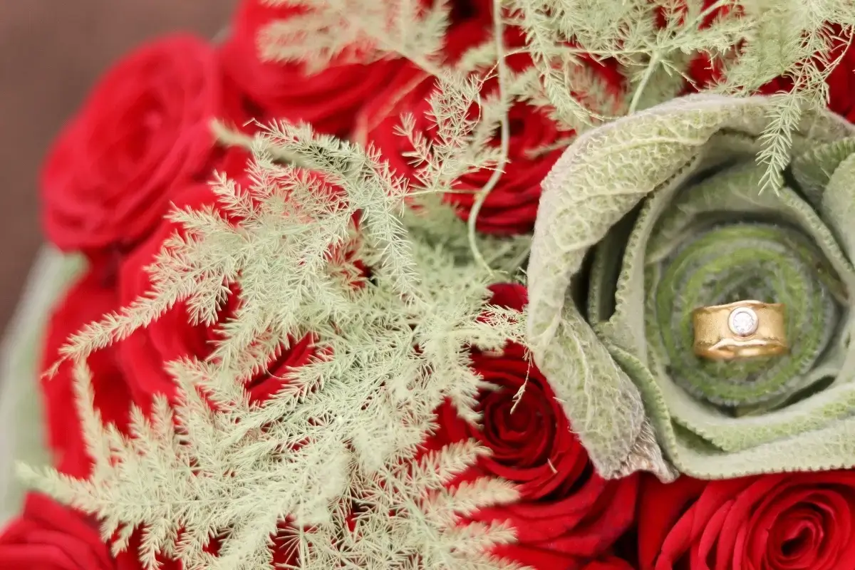 Gros plan d'un bouquet de roses rouges avec une rose en feuillage texturé abritant une bague de fiançailles par Cindy Gunther