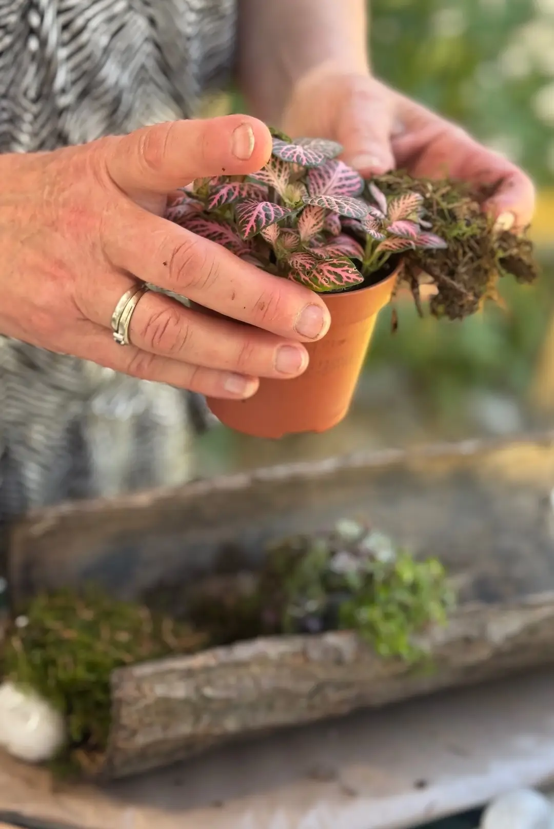 Mains d'une participante manipulant une plante dans un atelier d'art floral animé par Cindy Gunther avec un support en écorce.