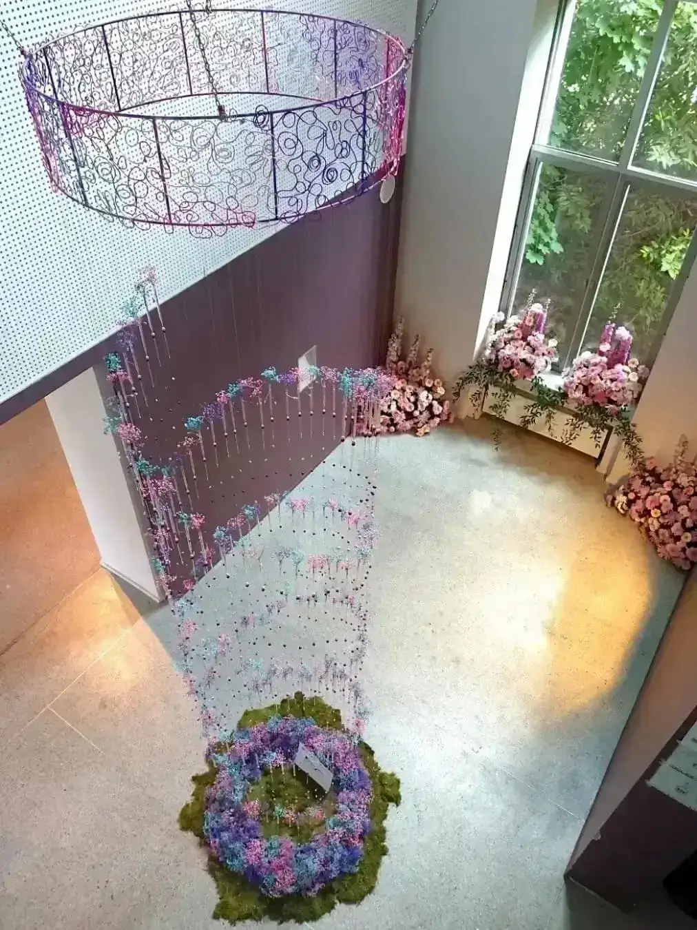 Vue en plongée d'un lustre monumental de 5 mètres de haut aux volutes en aluminium et aux teintes parme, rose et mauve, orné de centaines de pipettes de gypsophile Réalisation Cindy Gunther