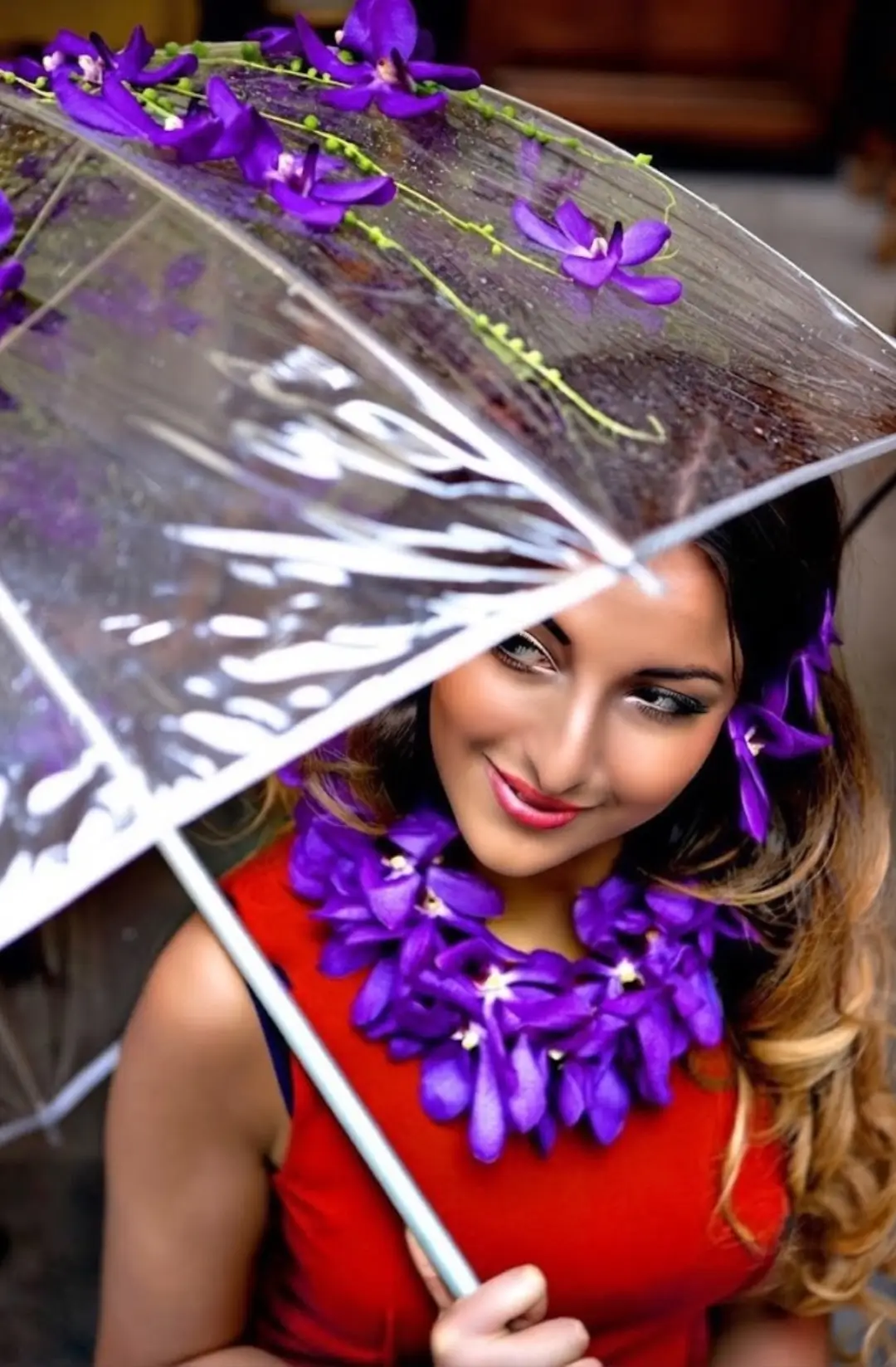 Gros plan d'un mannequin souriant portant une robe orangée, tenant un parapluie transparent orné d'orchidées Vanda violettes customisé par Cindy Gunther